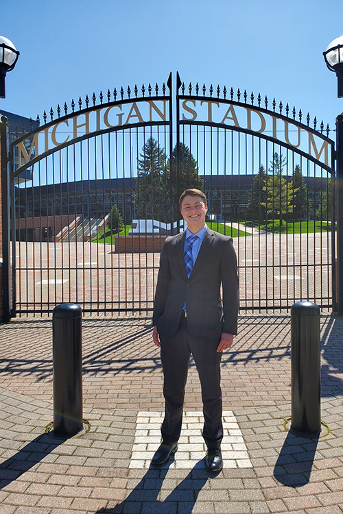 Connor Raines in business suit stands outside Michigan stadium on a sunny day