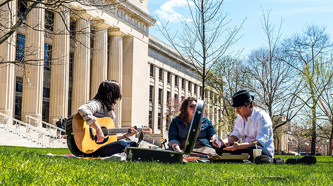 Students playing music resting on the lawn before Angell Hall