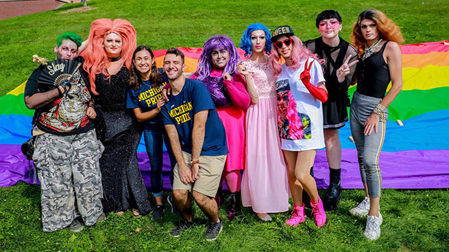 Students and drag queens in front of rainbow flag