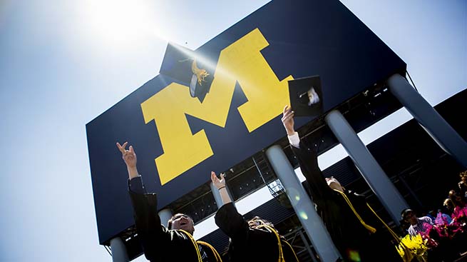 Grads throwing caps in front of Michigan Stadium